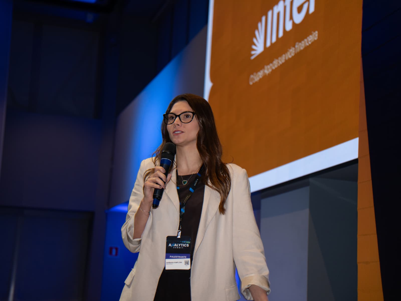 Bárbara Pamplona palestrando no Analytics Summit, com o painel do Inter ao fundo.